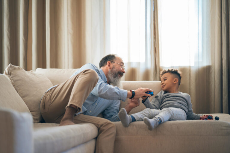 Grandfather and grandson playing with toy cars on a couch.